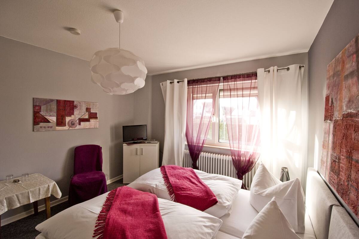 A modern hotel room with a bed, a television, a table with glasses, and a chair.