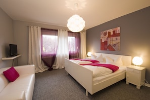 Quarto de hotel moderno com cama, mesas de cabeceira, televisão e um quadro na parede.