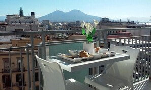 A balcony with a table set for two, overlooking a cityscape with buildings and a mountain in the background. - B&B Locanda Mediterranea (Naples)