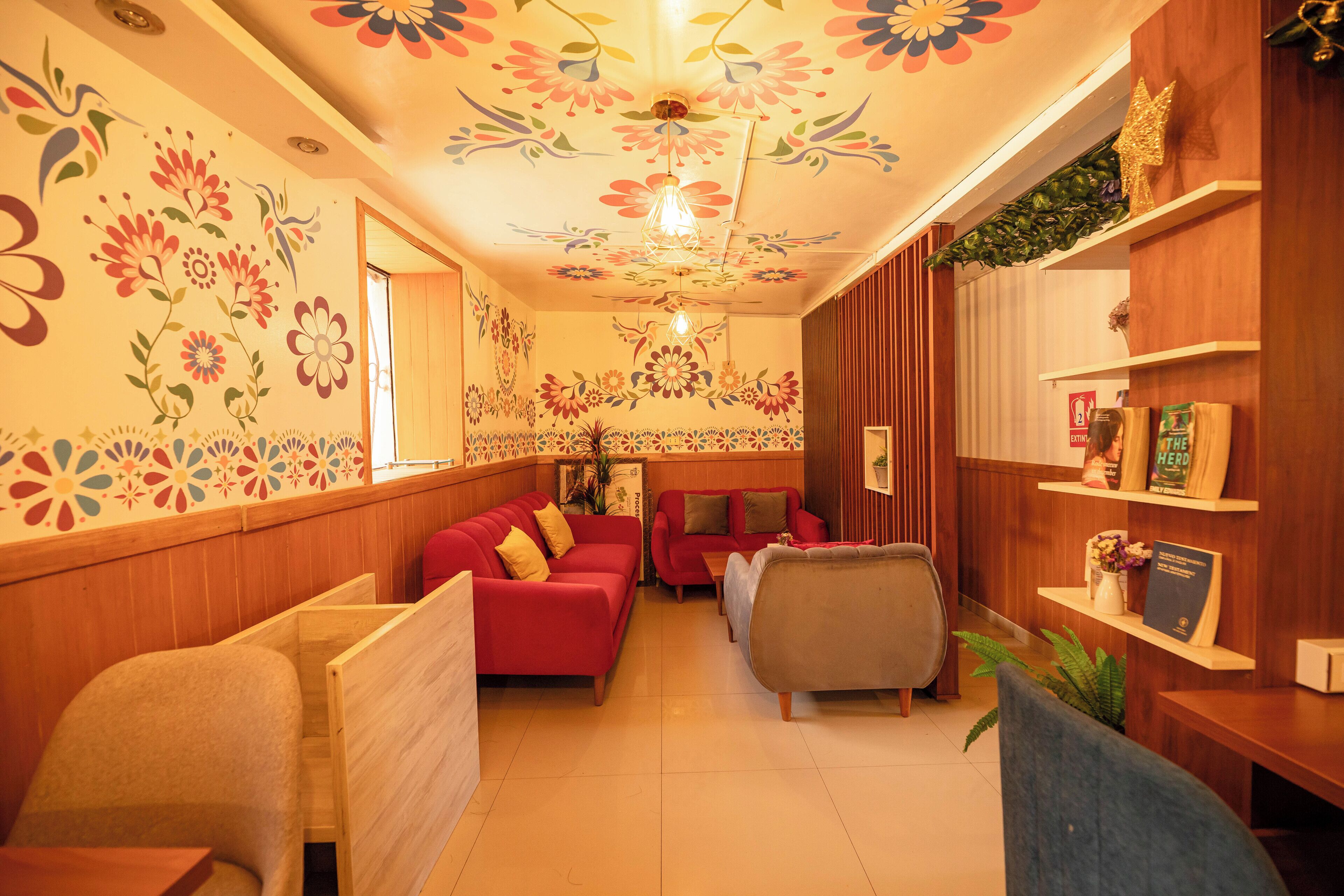 Een hotel lobby met houten lambrisering, rode banken, een houten receptiebalie en decoratieve bloemkunst aan het plafond.