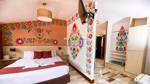 A hotel room with a large bed, a red chair, a wooden nightstand, and a wall with colorful floral patterns. - Mayu Boutique Hotel (Cusco)
