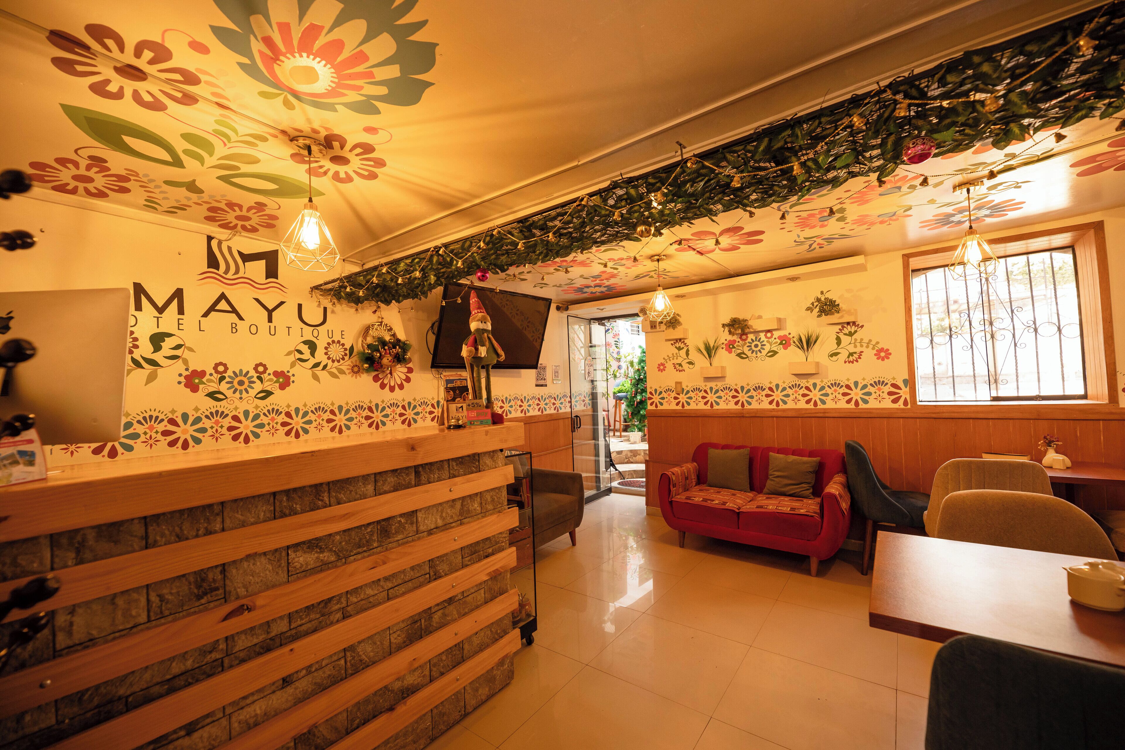 A hotel reception area with a wooden reception desk, a red sofa, and a dining area with a table and chairs.