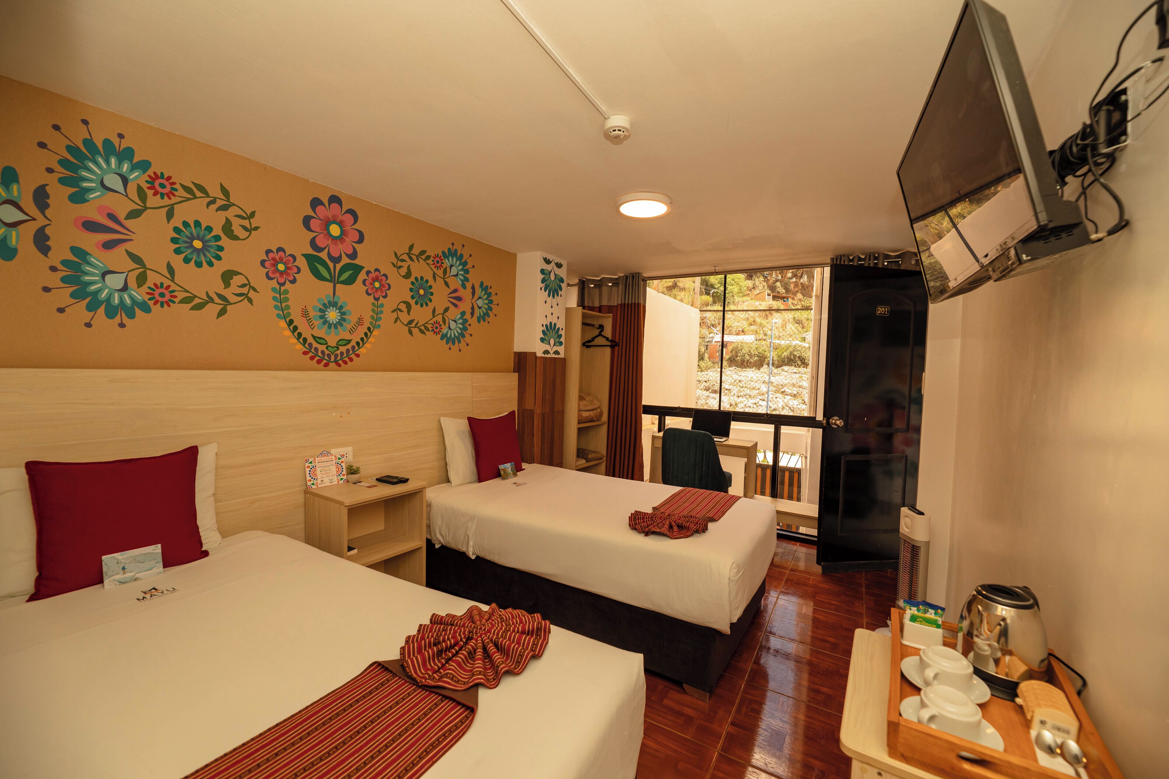 A hotel room with two beds, a TV, a desk with a coffee maker, and a balcony with a view.