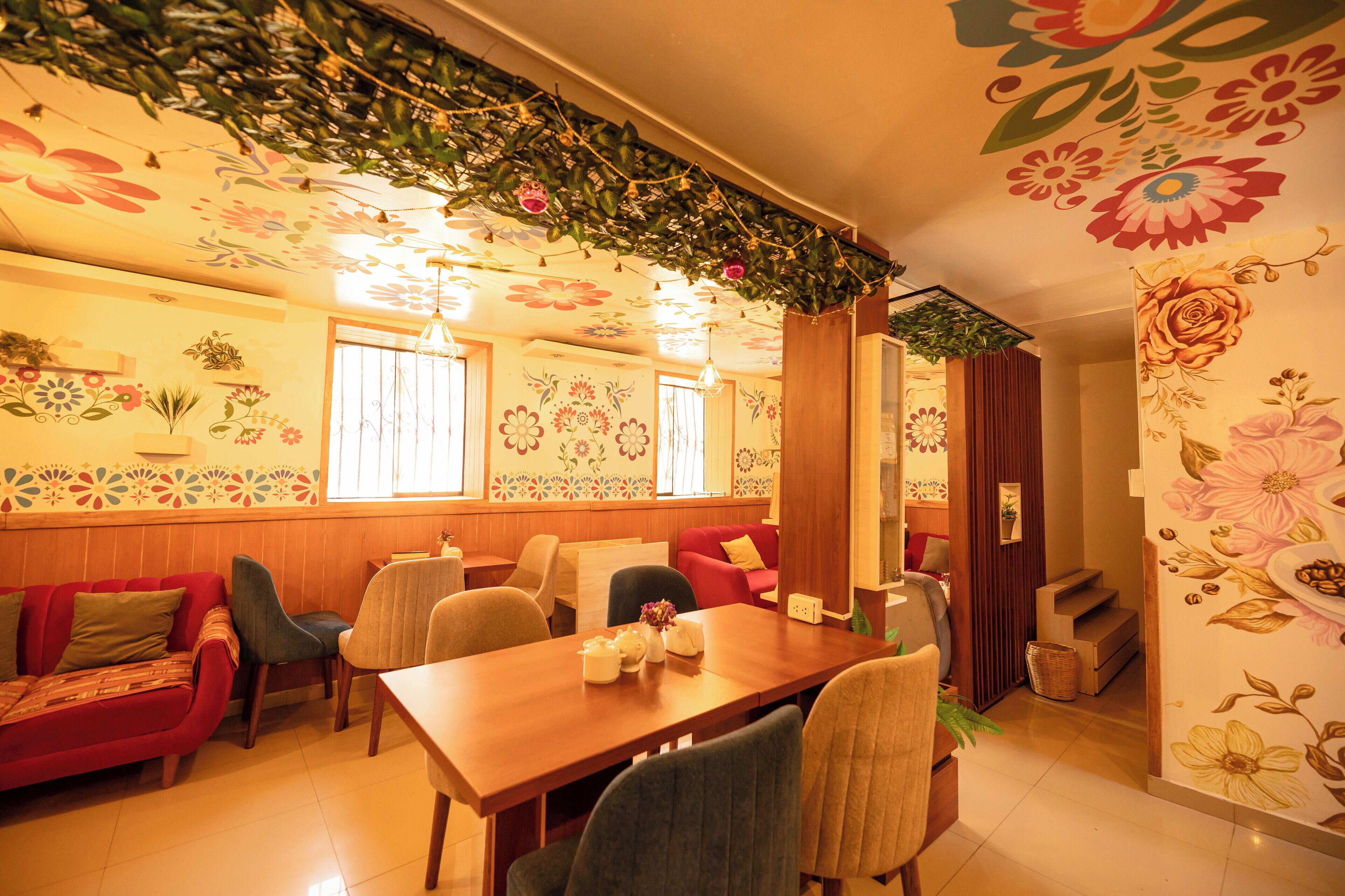 A dining area with a wooden table, chairs, and a red sofa. There are floral patterns on the walls and ceiling.