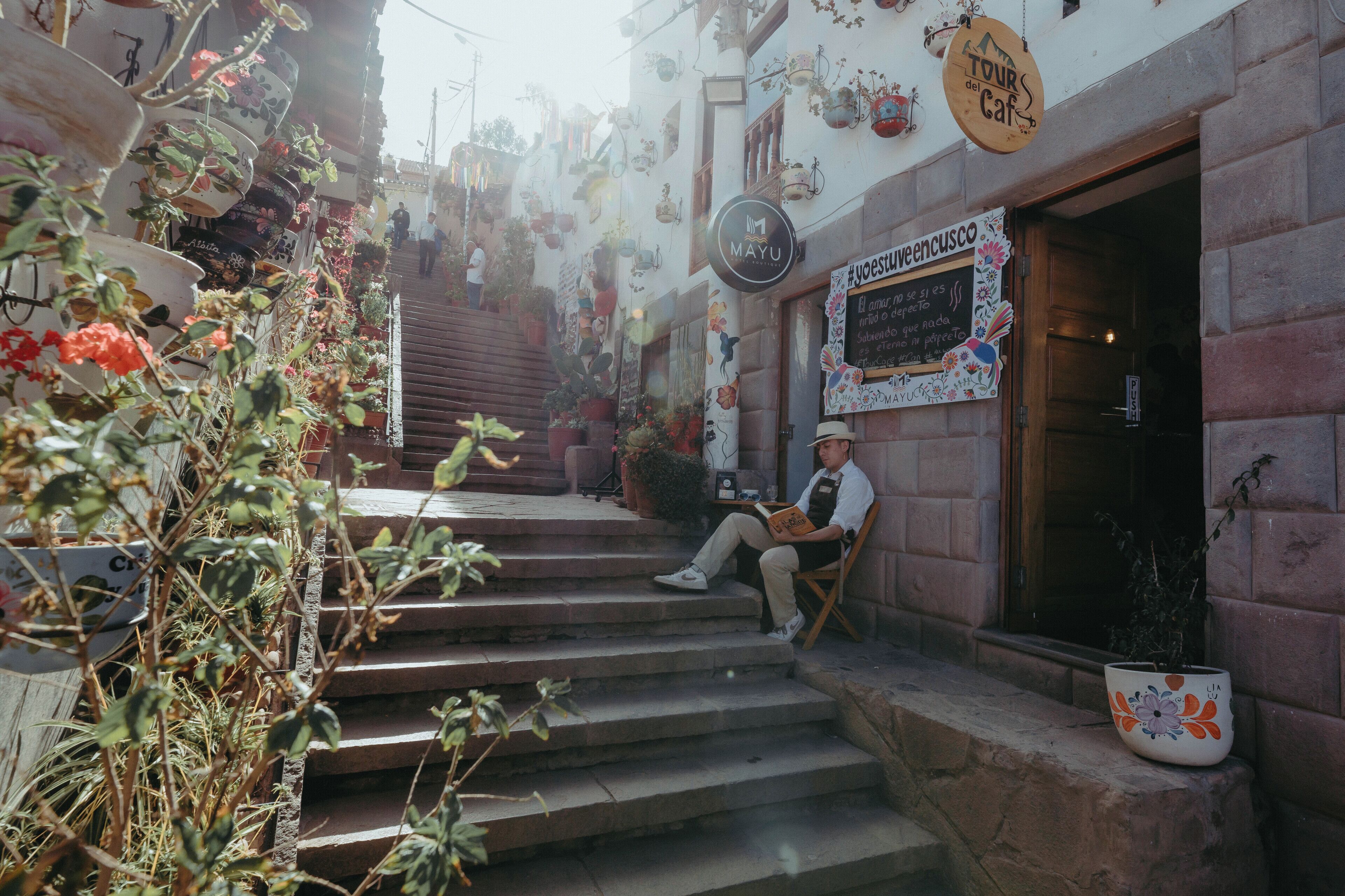 A man sitting on a bench outside a cafe with a sign reading "MAYU" and another sign with "TOURS del Caf".