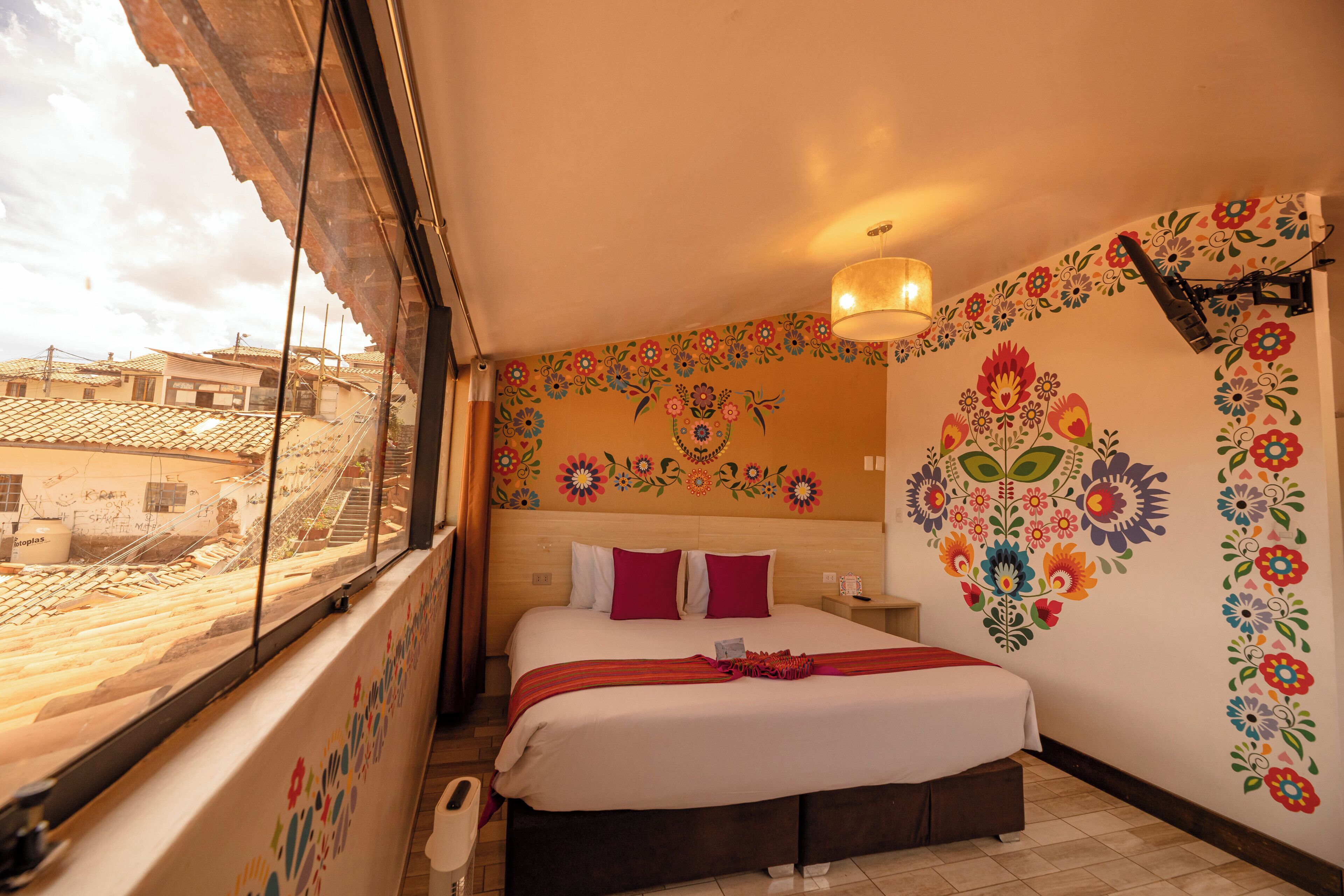 Quarto de hotel com cama, janela com vista para edifícios e parede decorada com flores.