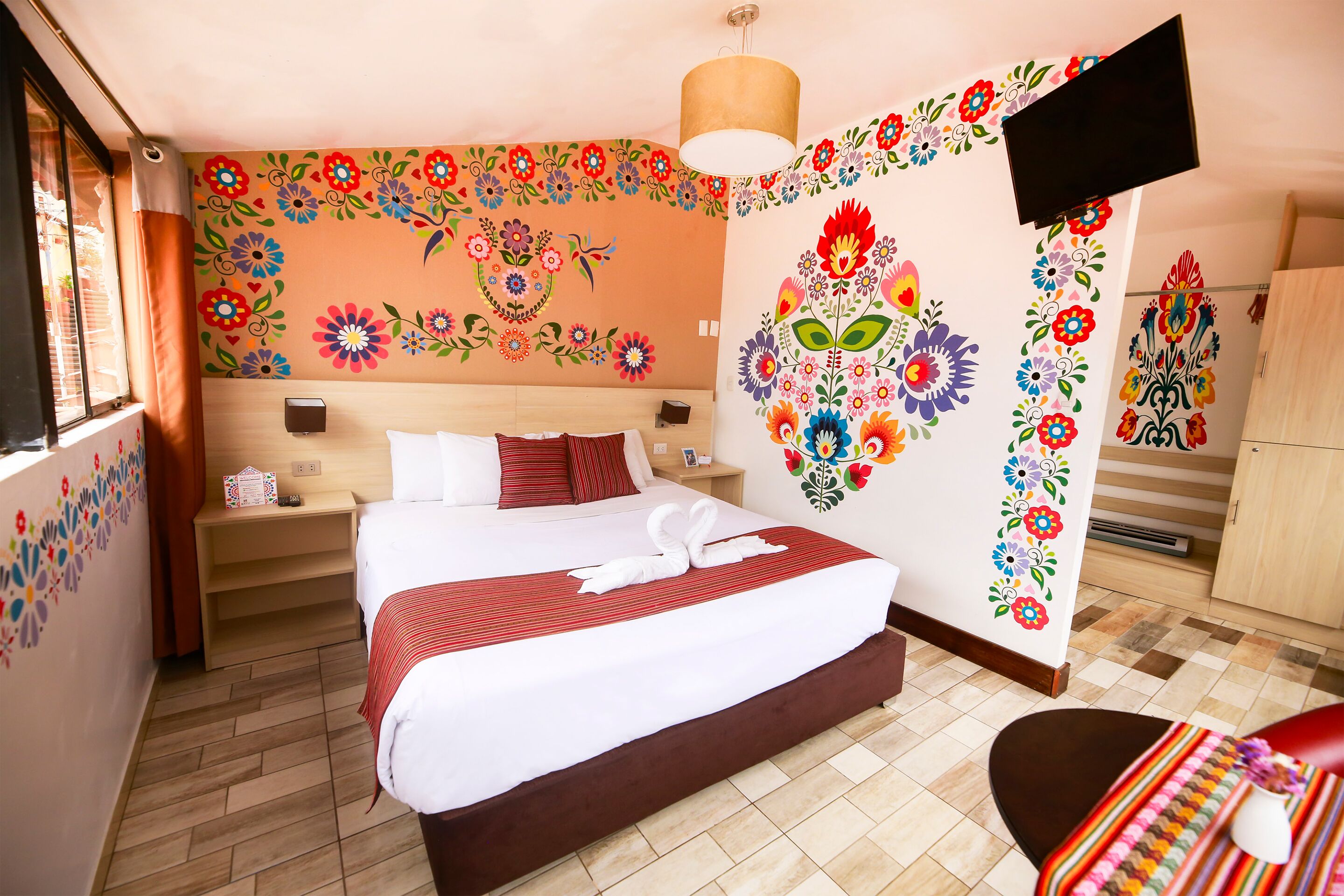 A hotel room with a large bed, a bedside table, a TV mounted on the wall, and a wooden wardrobe.