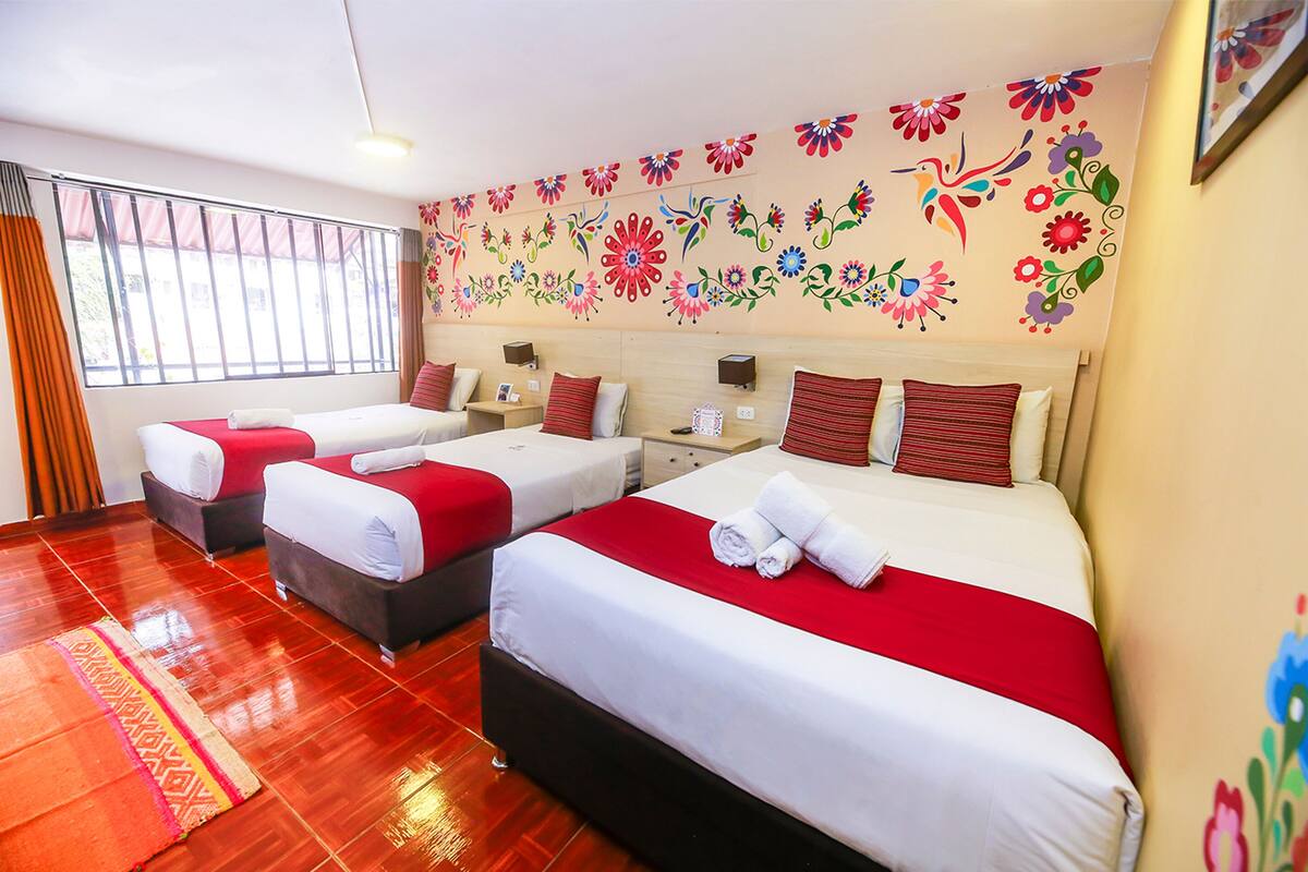 Une chambre d’hôtel avec trois lits, chacun doté de draps rouges et blancs, et une fresque florale sur le mur.