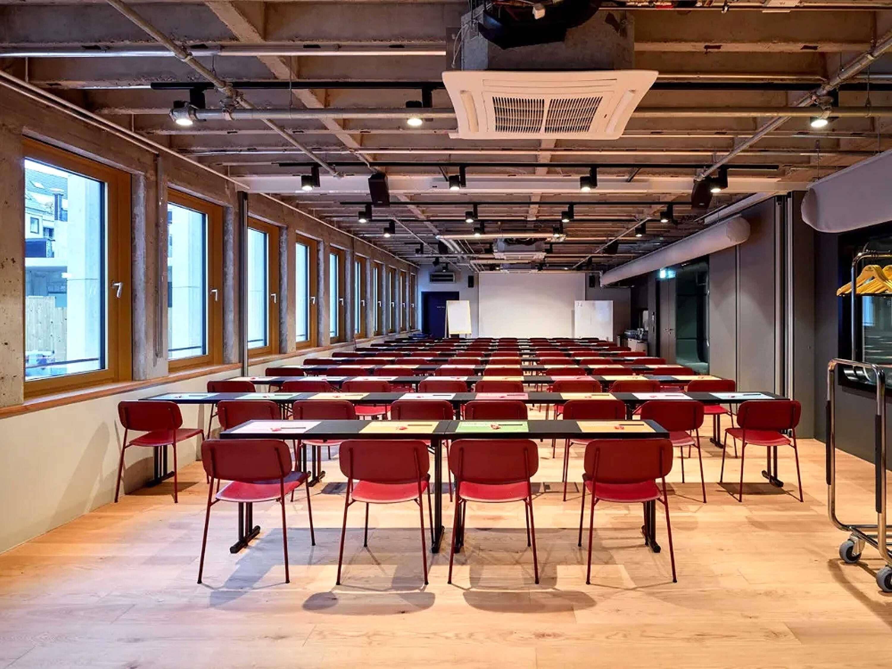 A conference room with rows of tables and chairs, large windows, and a projector on the ceiling.