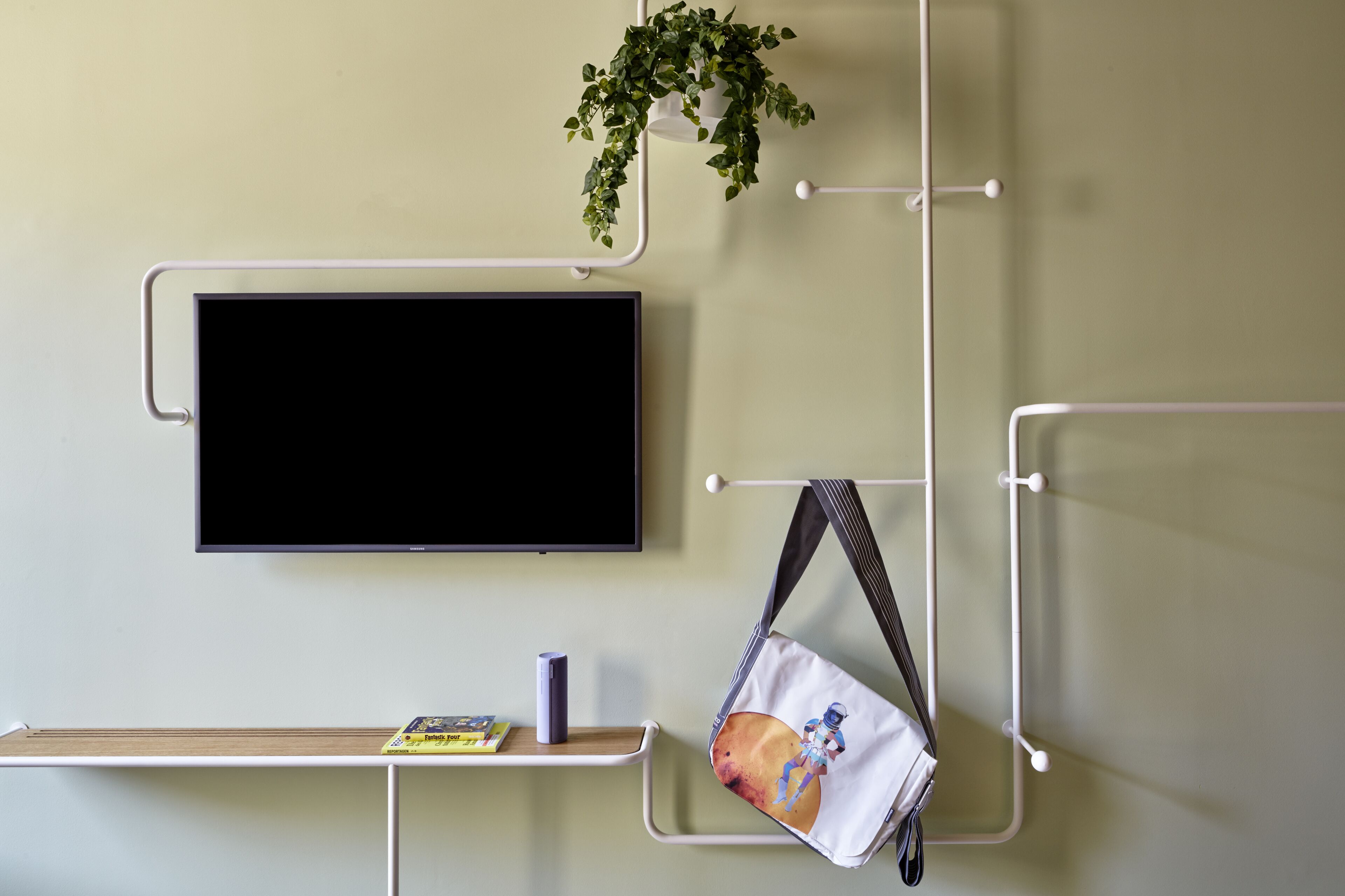 A wall-mounted TV, a shelf with a book and a cup, and a hanging bag with a space-themed design.