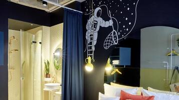 Een moderne hotelkamer met een glazen douchecabine, een bed met witte beddengoed en een muurschildering van een astronaut.
