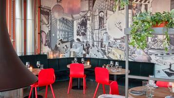 Interior de restaurante con sillas rojas, un mural de un paisaje urbano y una planta colgante.