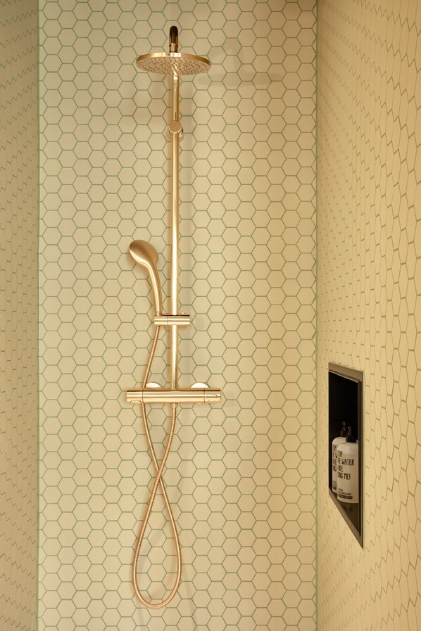 A shower with a gold finish, a handheld showerhead, and a wall-mounted control panel.