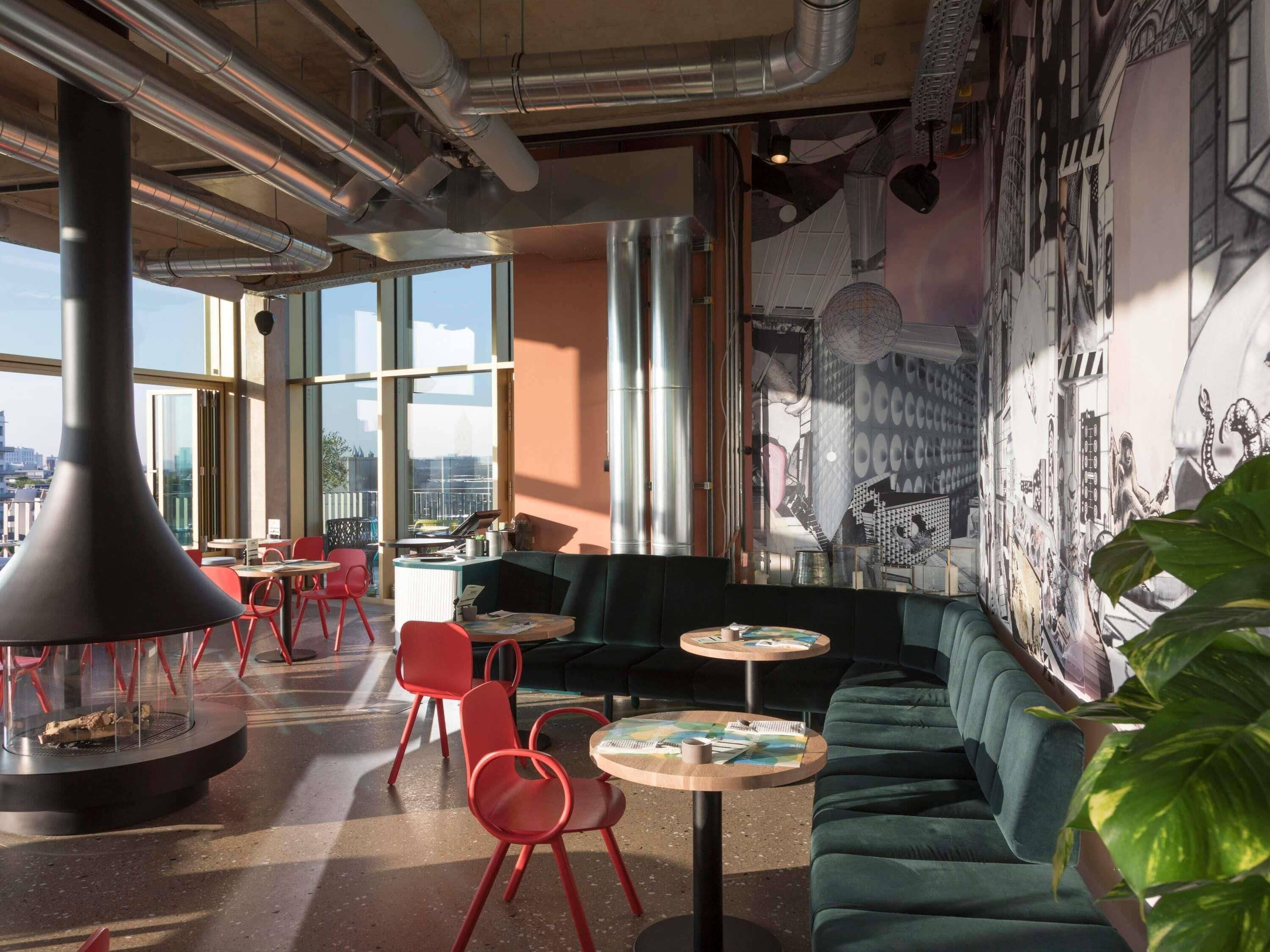 Un intérieur moderne avec un canapé vert, des chaises rouges et une fresque murale.