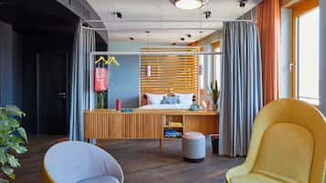 Habitación de hotel moderna con cama, mesita de noche, dos sillas, un espejo y una planta en maceta.