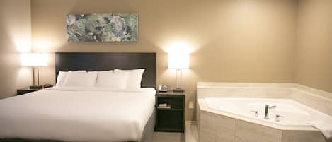 Habitación de hotel con una cama grande, dos lámparas de noche, una mesita de noche, un cuadro en la pared y un baño separado con bañera.