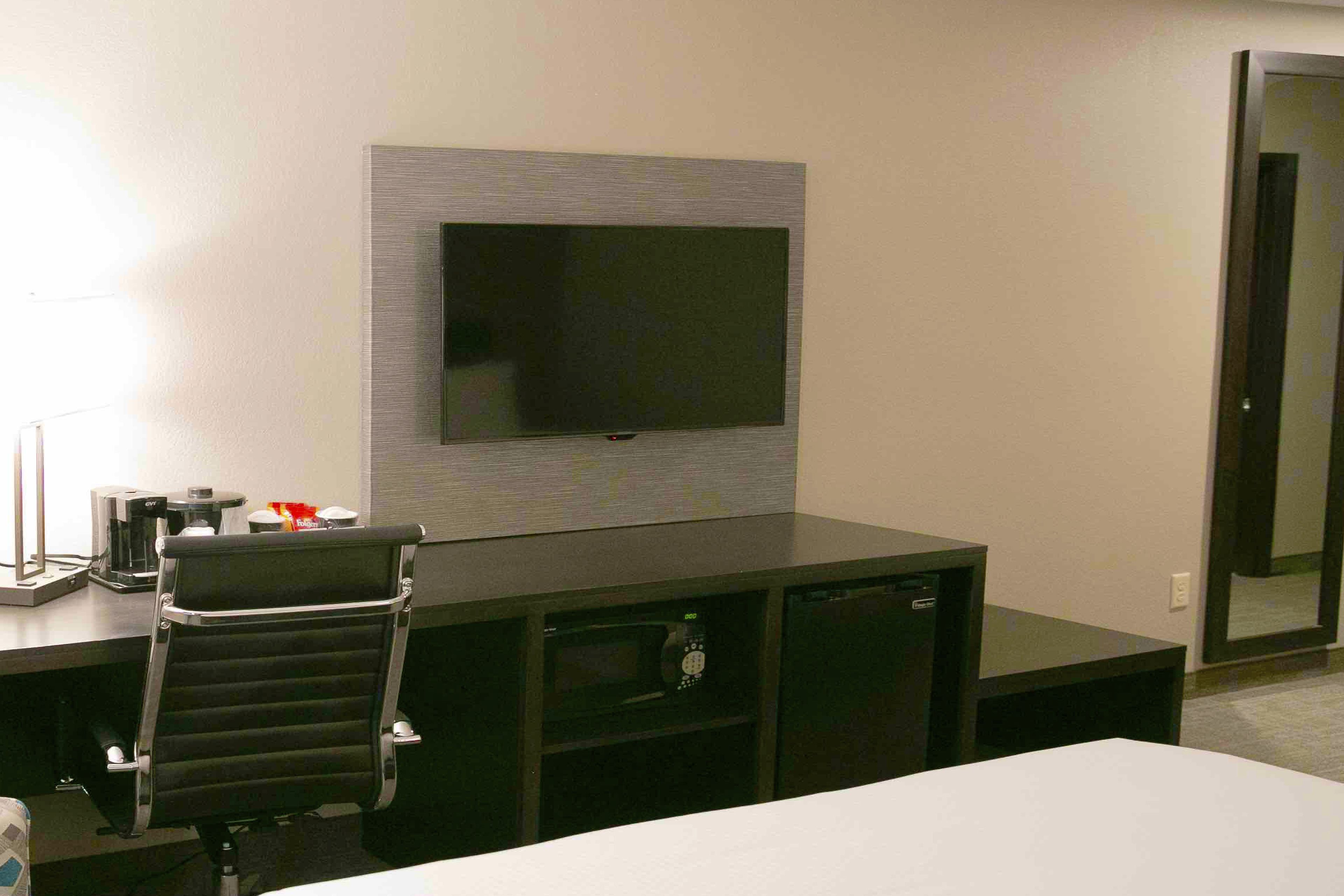 A hotel room with a flat-screen TV mounted on the wall, a desk with a chair, a microwave, and a coffee maker.