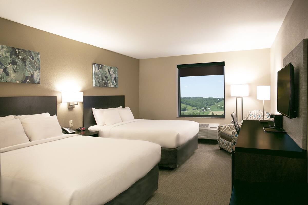 Habitación de hotel con dos camas, un ventanal con vistas, un televisor de pantalla plana y obras de arte en las paredes.