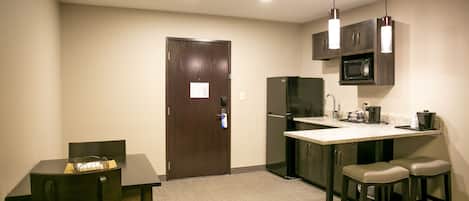 Una cocina compacta con una mesa de madera oscura, dos taburetes de bar, un refrigerador, un microondas y lámparas colgantes.
