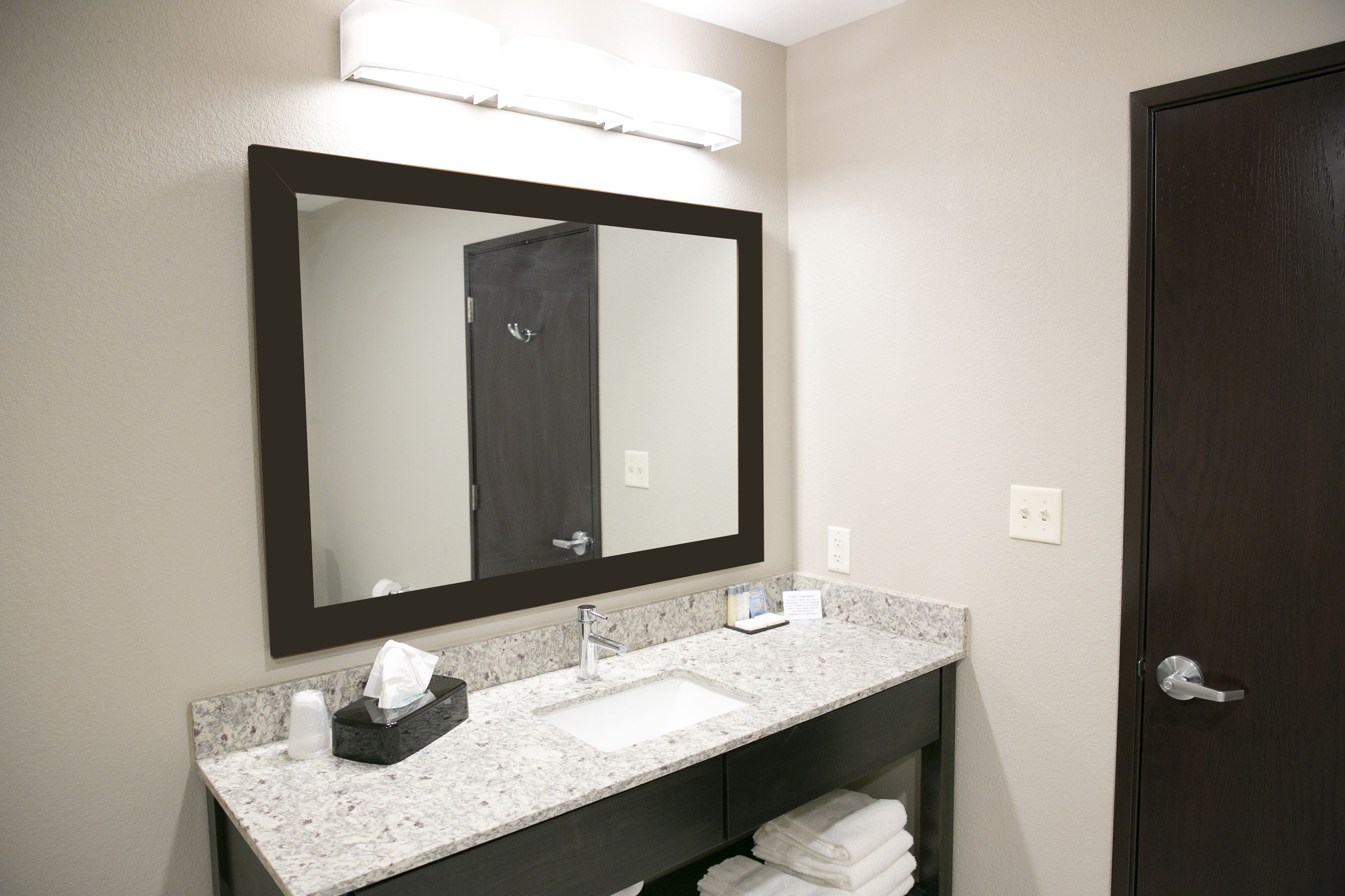 A bathroom with a large mirror, a sink, and a dark door.