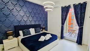 A bedroom with a bed, bedside tables, a lamp, a hanging coat rack, and a view of the outside. - Maschio Angioino Suite (Naples)