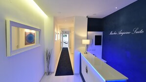 A modern hotel lobby with a reception desk, a framed artwork on the wall, and a hallway leading to other rooms. - Maschio Angioino Suite (Naples)