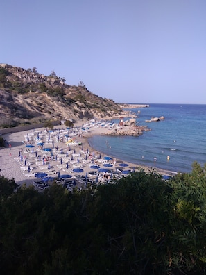 A beach with rows of sun loungers and umbrellas, rocky cliffs, and the sea.