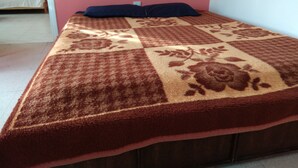 Una cama con una colcha estampada, un almohadón oscuro y un cabecero de madera.