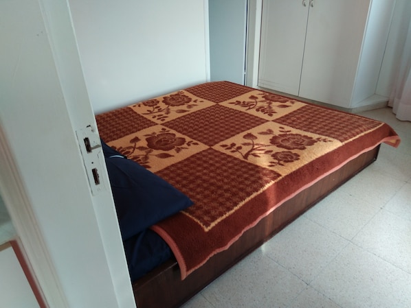 A small, single-bed room with a patterned bedspread, a dark blue pillow, and a wooden headboard.