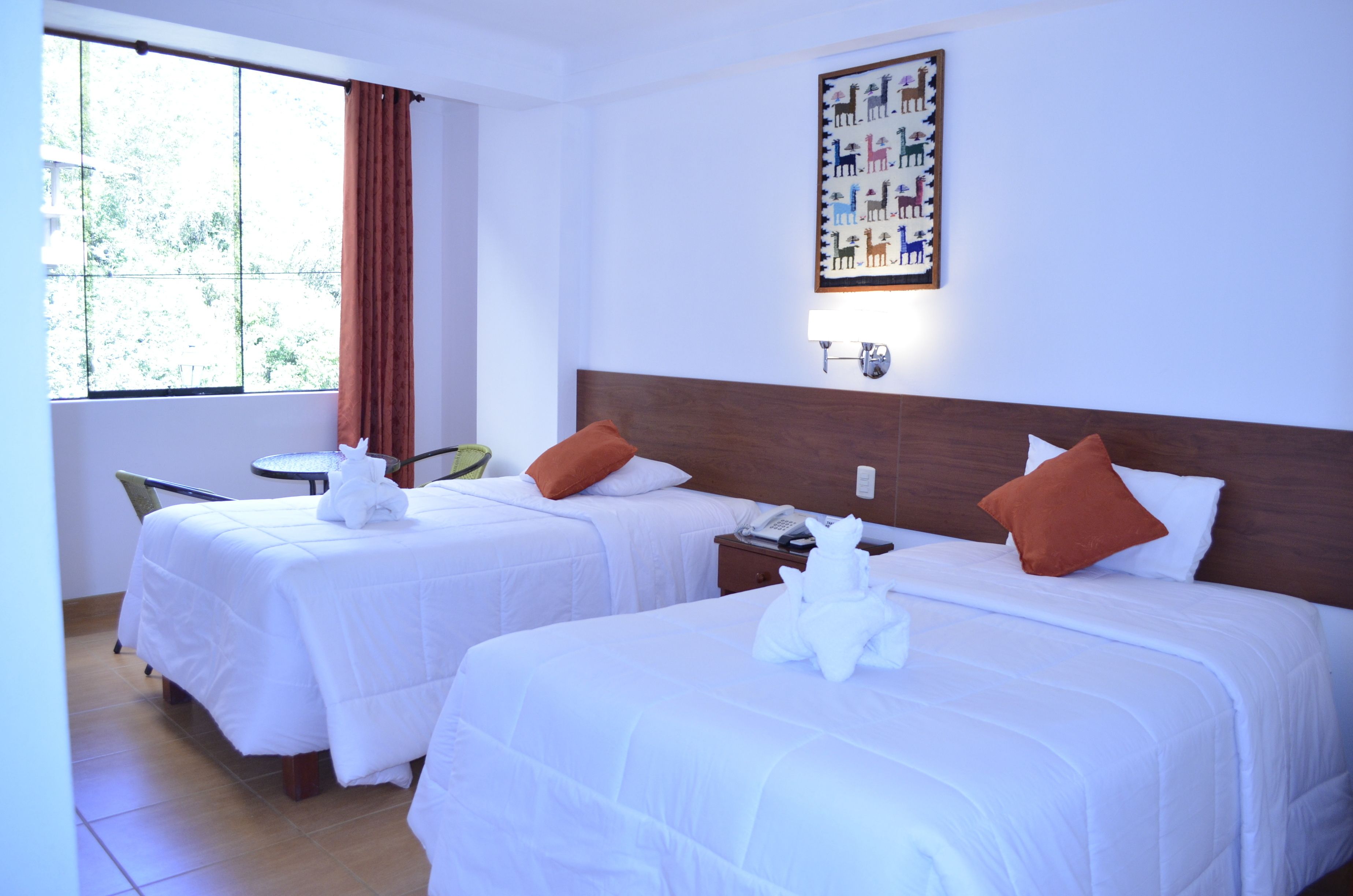 Quarto de hotel com duas camas, uma janela com cortinas, uma obra de arte na parede e uma pequena mesa com uma cadeira.