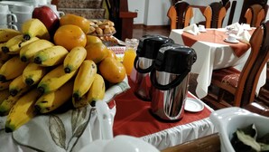 A breakfast setup with bananas, oranges, and a coffee pot on a table. - Viandina Machupicchu (Machu Picchu)