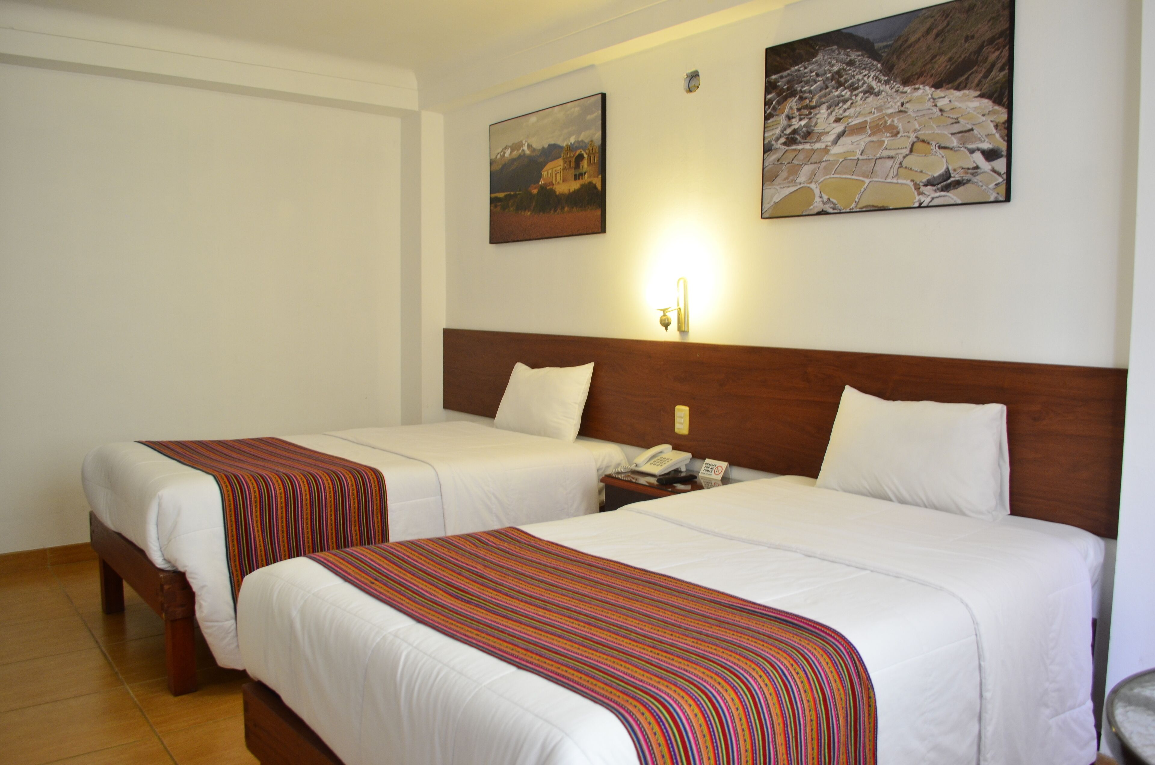 Habitació d'hotel amb dos llits, ambres de fusta, roba de llit blanca, mantilles amb ratlles, una nit de nit amb un telèfon i dos quadres emmarcats a la paret.