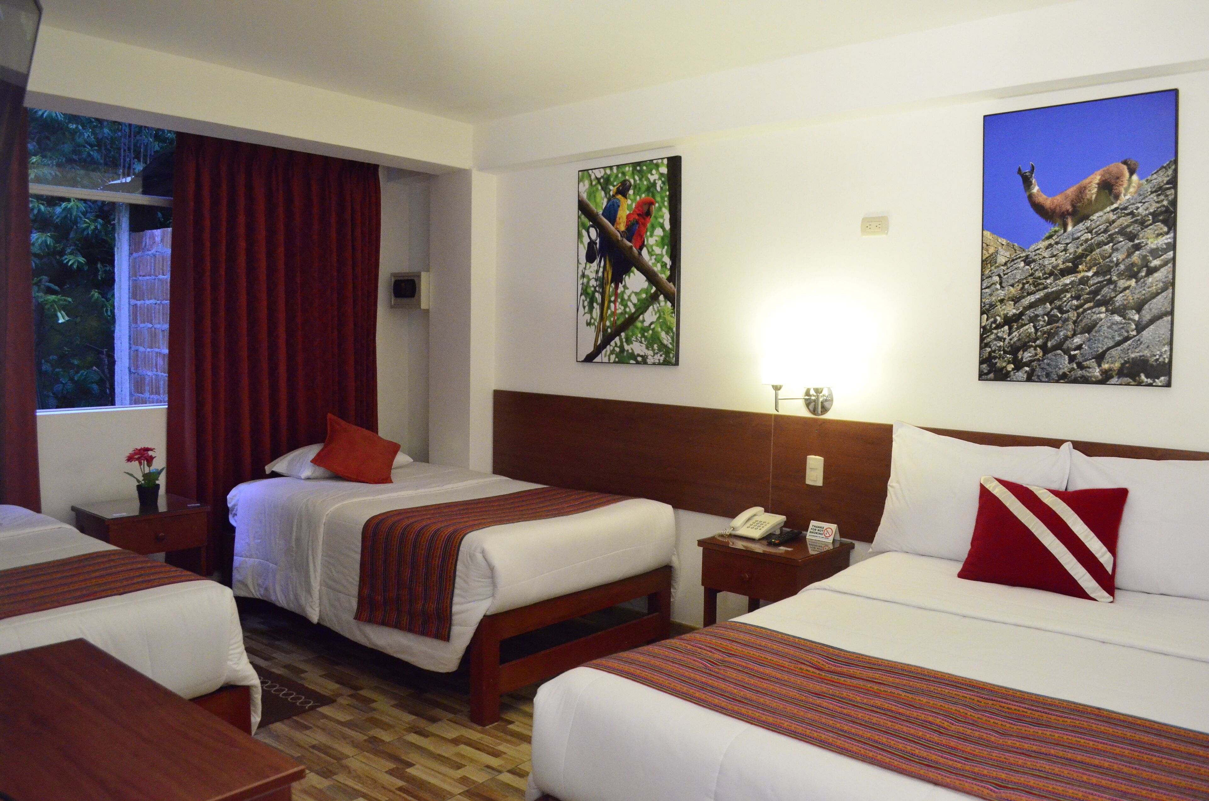 Una habitación de hotel con dos camas, un cabecero de madera, una mesita de noche con teléfono y una ventana con cortinas rojas.