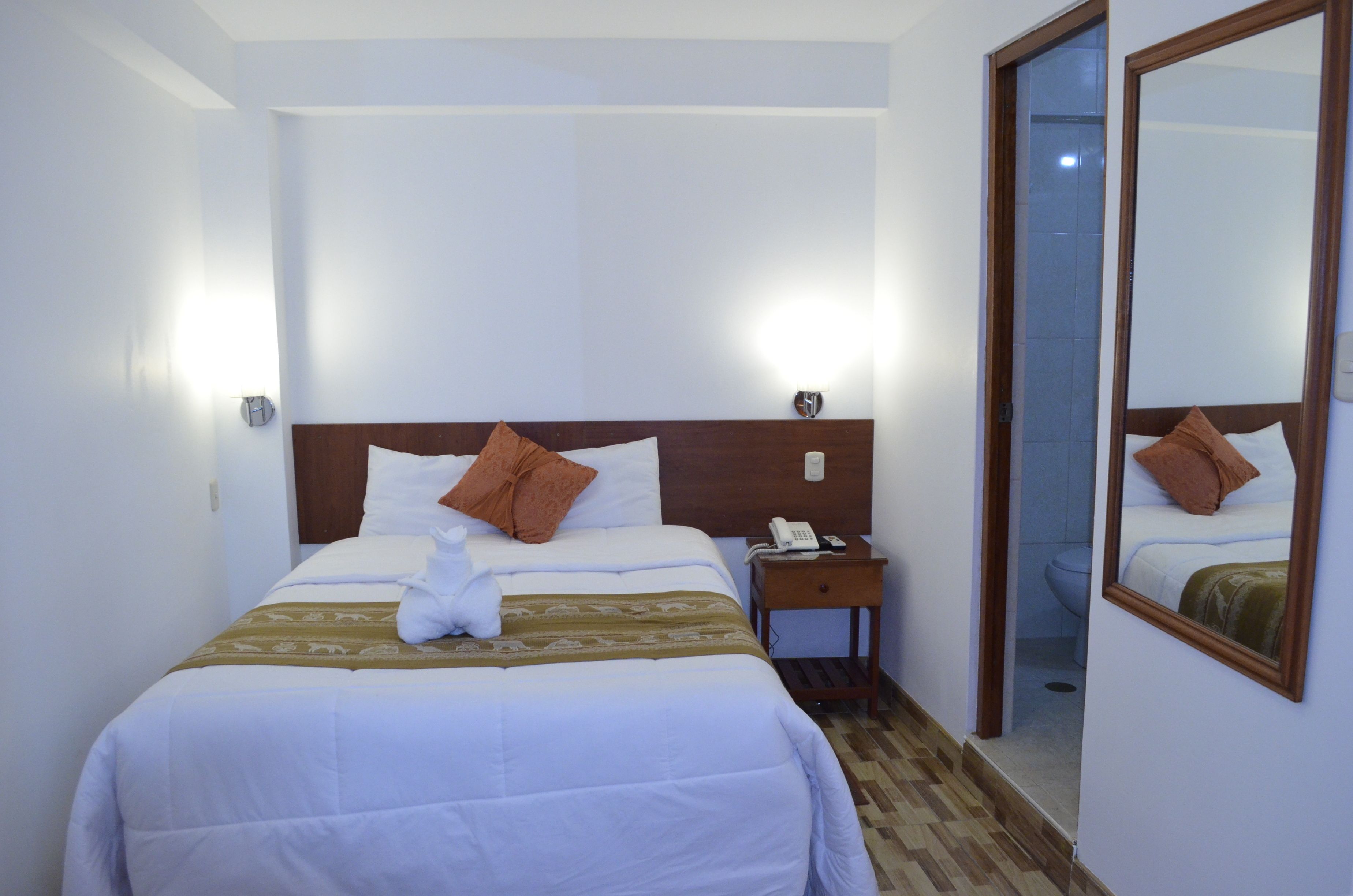 A hotel room with a large bed, a nightstand with a phone, a mirror, and a door leading to a bathroom.