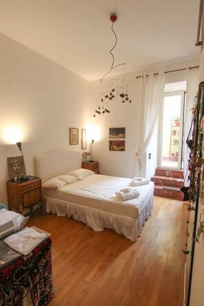 Quarto com cama, mesas de cabeceira, cômoda e janela com cortinas.