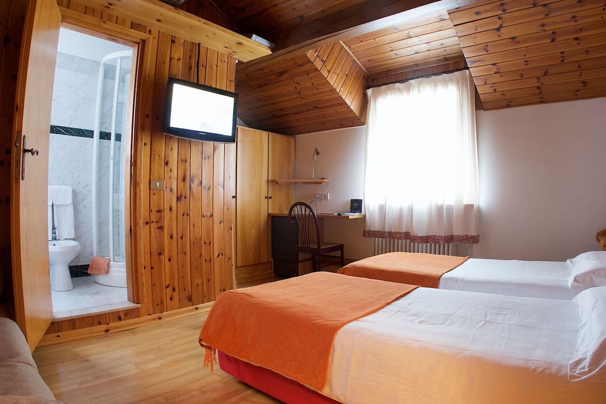 A wooden-paneled room with two beds, a TV, a shower, and a toilet.