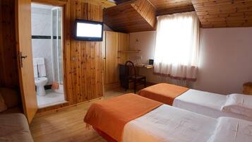 A wooden cabin room with two beds, a desk, a chair, a television, and a bathroom visible through an open door.