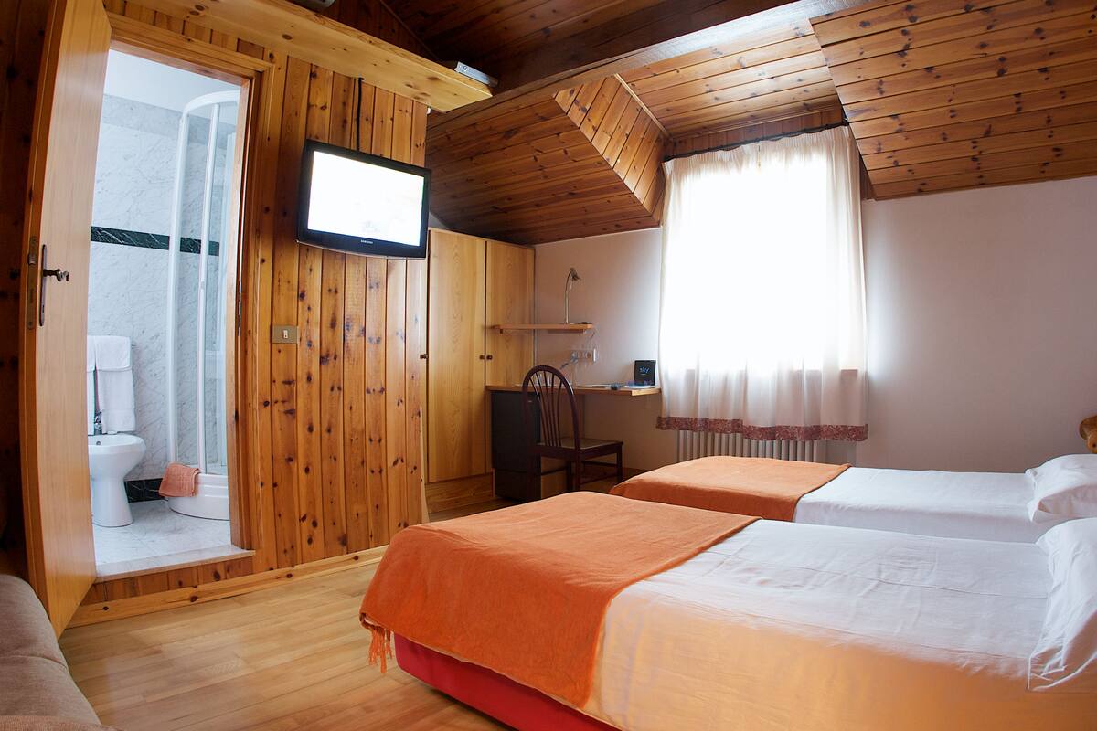 A wooden-paneled room with two beds, a television, a shower area, and a desk.