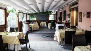An indoor dining area with tables covered in tablecloths, wicker chairs, and a central decorative element on the floor. - Locanda San Lorenzo (Alpago)