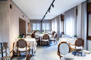 Un espace repas moderne avec des tables rondes et des chaises en osier, de grandes fenêtres avec des rideaux et un mur en bois.