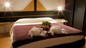 A neatly made bed with a purple blanket, white pillows, and a bouquet of flowers. There is a small bedside table with a lamp and a phone. - Locanda San Lorenzo (Alpago)
