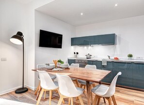 A modern kitchen with dark cabinets, a wooden dining table, and white chairs. - Sorrento Lux Suites - Blue (Sorrento)