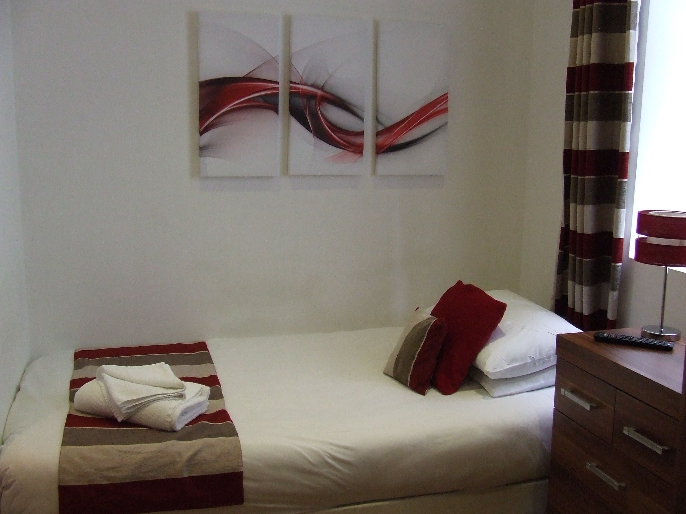 Habitación de hotel con una cama individual, una mesita de noche con lámpara y un cuadro abstracto colgado en la pared.