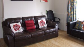Ein Wohnzimmer mit einem braunen Ledersofa, einem schwarzen Bürostuhl und zwei Kunstwerken an der Wand.