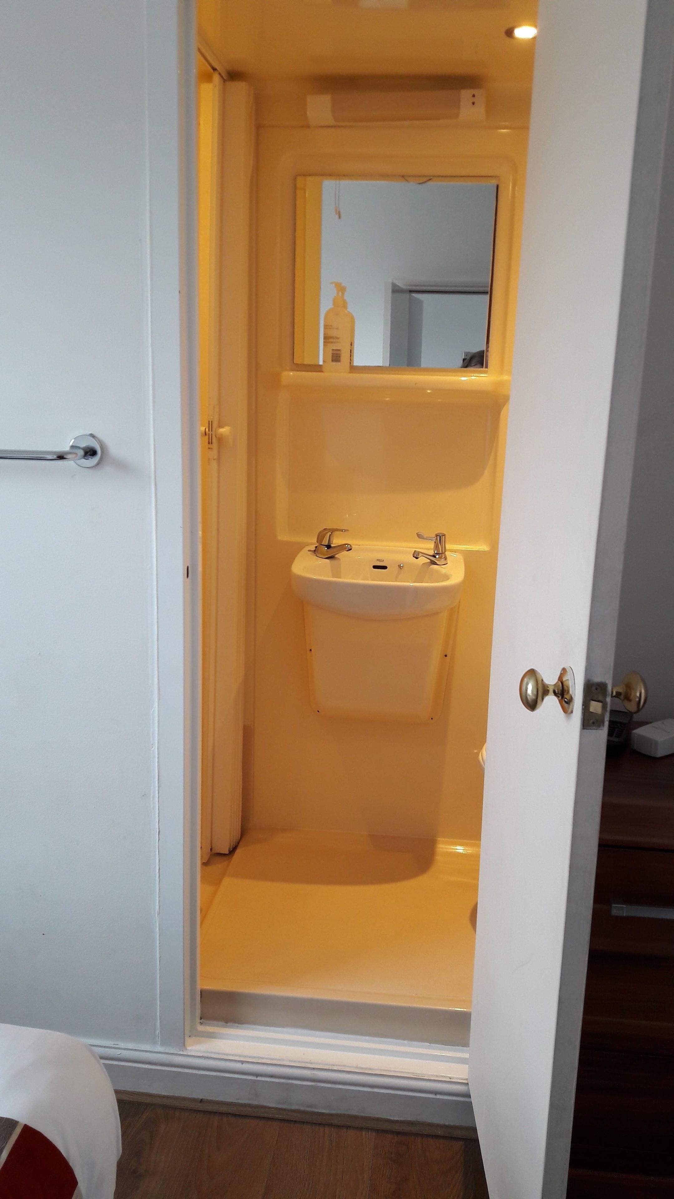 Un baño con lavamanos blanco, un espejo encima y una puerta con manija.
