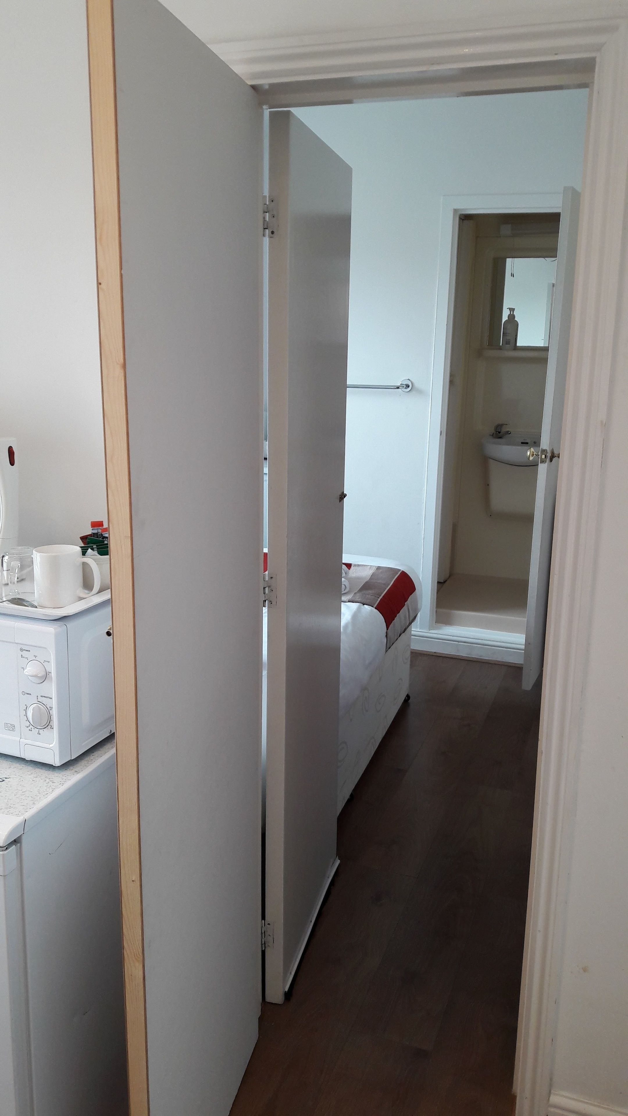 A hotel room with a bed, a bedside table with a coffee maker, and a bathroom visible through an open door.