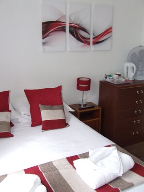 A hotel room with a bed, a nightstand, a dresser, and a wall-mounted artwork. - Alexandra Guest House (Hemel Hempstead)