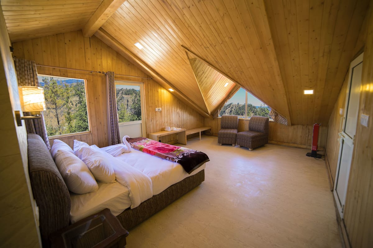 A bedroom with a wooden ceiling, a bed with white linens, a bench, and a chair.