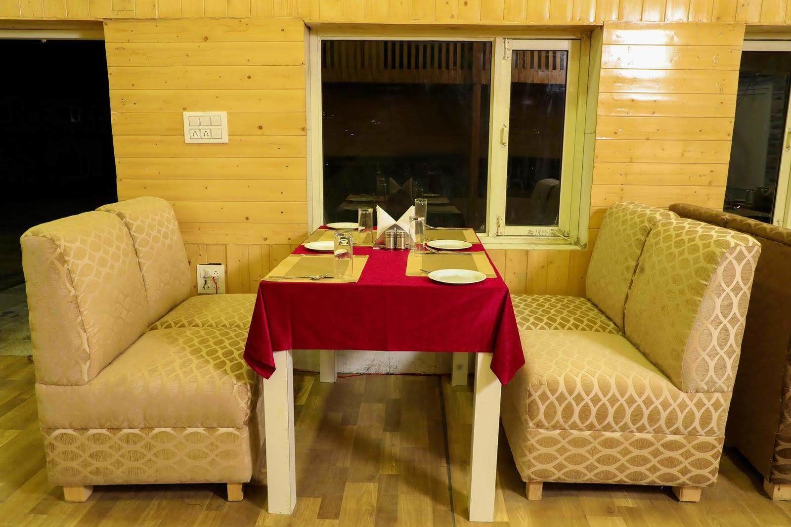 A cozy dining area with a wooden interior, a table set for two with a red tablecloth, and two patterned armchairs.