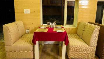 A cozy dining area with a wooden interior, a table set for two with a red tablecloth, and two patterned armchairs.
